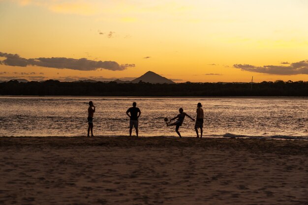 Silueta de personas jugando al fútbol en la playa al atardecer en Noosa, Queensland, Australia