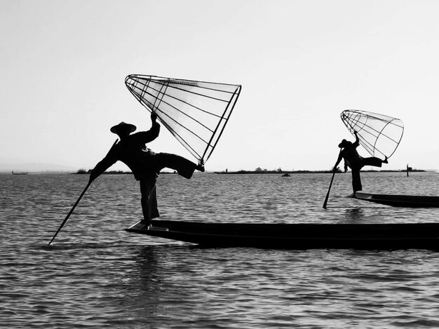 Silueta de personas pescando en un barco en el mar contra un cielo despejado