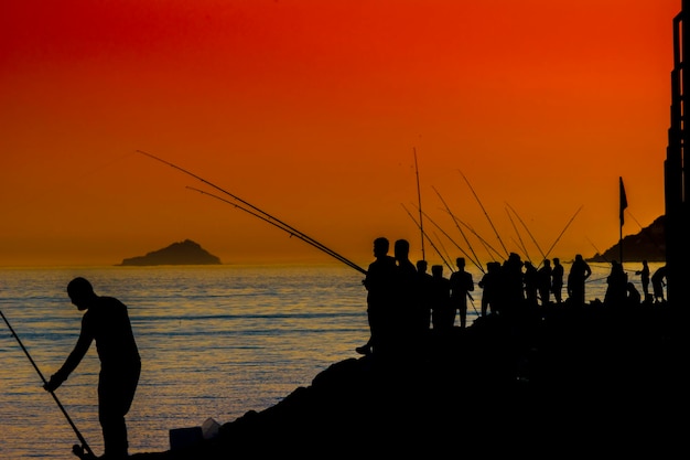 Foto silueta de personas pescando durante la puesta de sol