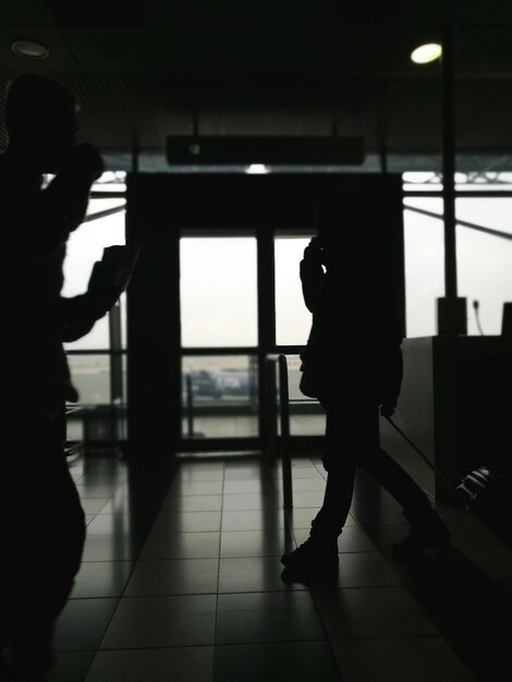 Silueta de personas de pie entrando o saliendo por el corredor del aeropuerto