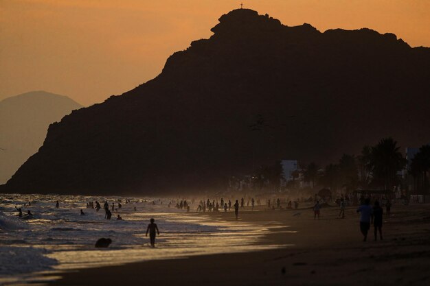 Silueta de personas en la playa contra el cielo durante la puesta de sol