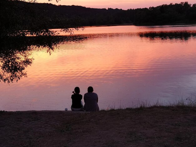 Silueta de personas sentadas en el lago contra el cielo durante la puesta de sol