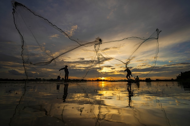 Silueta de pescador en barco de pesca con red en el lago al atardecer, Tailandia
