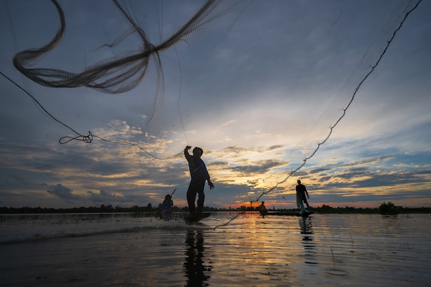 Silueta de pescador en barco de pesca con red en el lago al atardecer, Tailandia