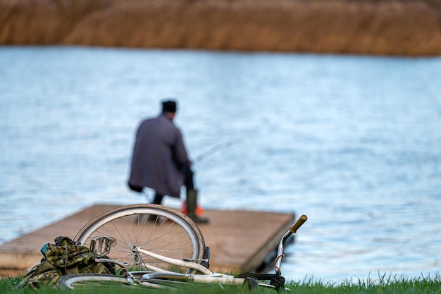 Silueta de un pescador con una caña de pescar en un puente de madera junto al río enfoque selectivo trasero