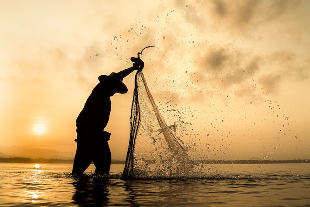 Silueta de pescadores con herramientas de pesca y durante el sol dorado brilla