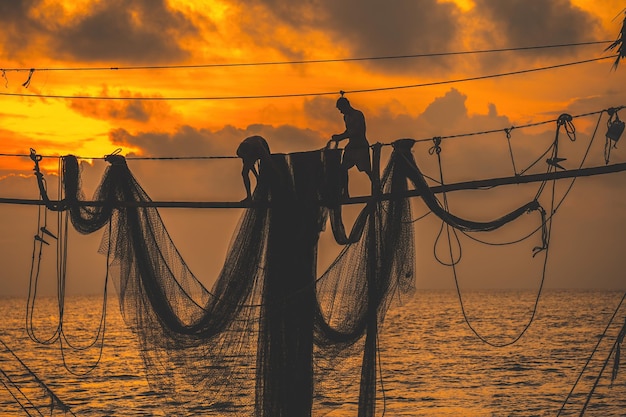 Silueta de pescadores lanzando redes en cañas de pescar al amanecer Los pescadores tradicionales preparan la red de pesca que la gente local llama Day hang khoi Concepto de pesca y vida cotidiana