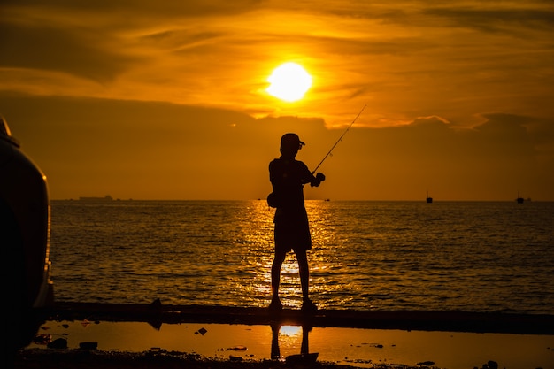 La silueta de los pescadores del retrato de la vida en el mar y la puesta de sol sobre el fondo por la noche