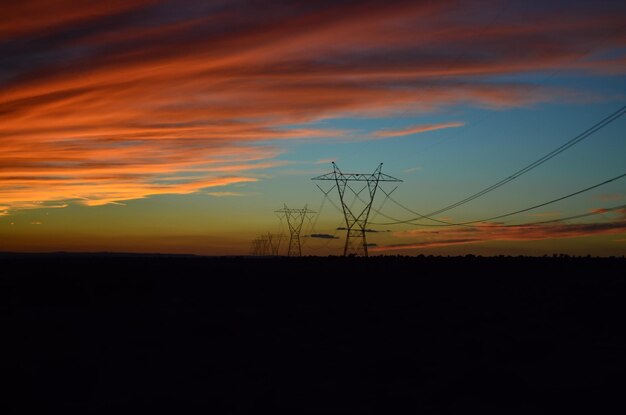 Silueta de pilares eléctricos contra el cielo nublado durante la puesta del sol