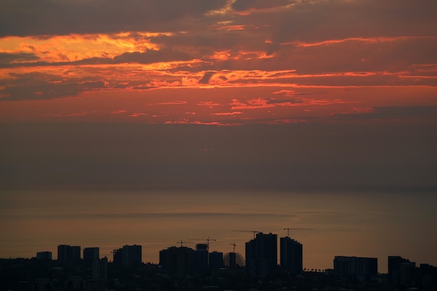 Silueta de rascacielos y área de construcción con puesta de sol cielo sobre el mar