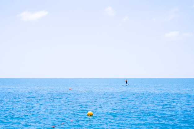 Foto silueta de servidores de pie sobre una tabla de surf en un mar en calma.