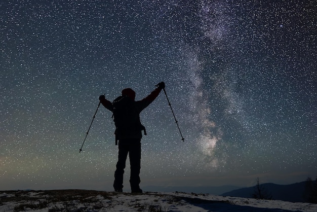 Silueta solitaria de un excursionista masculino adulto en la cima de una montaña cubierta de nieve antes del amanecer Cielo estrellado en el fondo