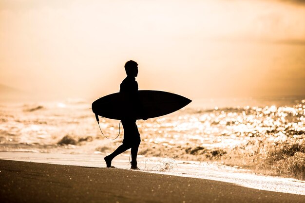 Silueta de un surfista en la playa contra el cielo durante la puesta de sol