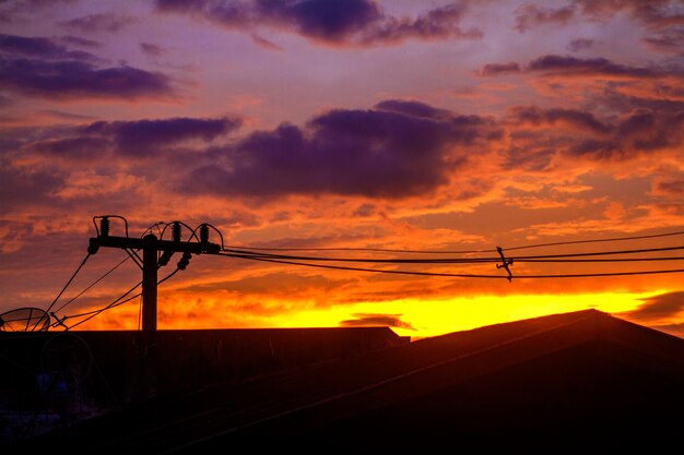 Foto silueta de una torre de electricidad contra un cielo dramático durante la puesta de sol