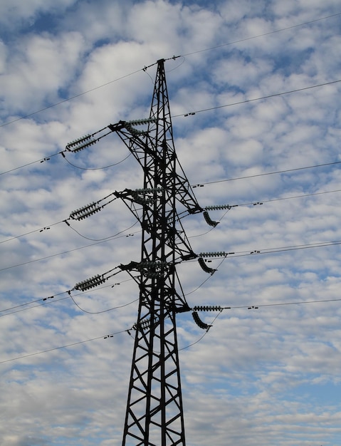 Silueta de la torre de la línea de alta tensión bajo las nubes en un cielo azul