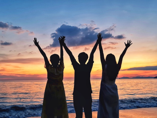 Silueta de tres amigos por la noche en la playa mirando el atardecer.