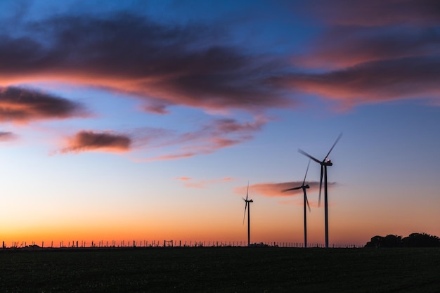 Silueta de tres molinos de viento modernos bajo una puesta de sol azulada en las afueras de Kiyu