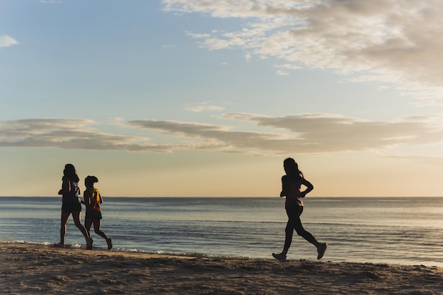 Silueta de tres mujeres trotando en la playa al amanecer.