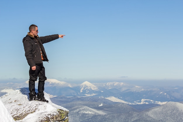 Silueta del turista solo que se coloca en la cima de la montaña nevada que disfruta de la vista y del logro en día de invierno soleado brillante.