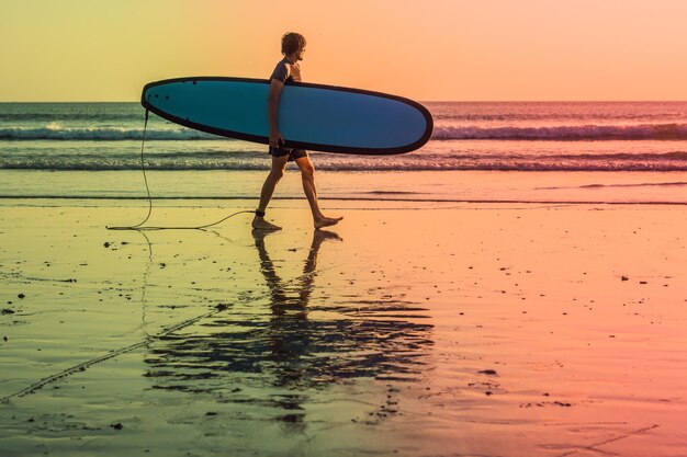 Silueta de vacaciones de un surfista que lleva su tabla de surf a casa al atardecer con espacio de copia.