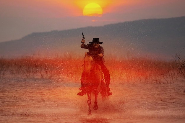 Foto silueta de un vaquero a caballo vadeando el agua al atardecer detrás de una montaña