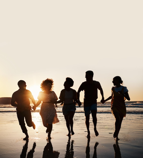 Silueta de verano y amigos tomados de la mano en la playa al atardecer para divertirse y viajar. Grupo de hombres y mujeres espaciales corriendo al aire libre en el agua con amor, apoyo y felicidad en vacaciones o vacaciones.