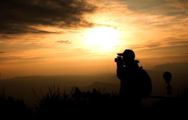 Silueta del viajero de la mujer que usa la cámara toma la foto sobre fondo hermoso de la puesta del sol