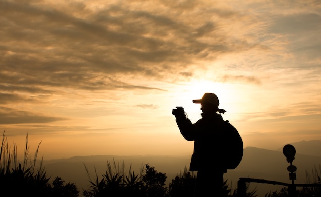 Silueta del viajero de la mujer que usa la cámara toma la foto sobre fondo hermoso de la puesta del sol