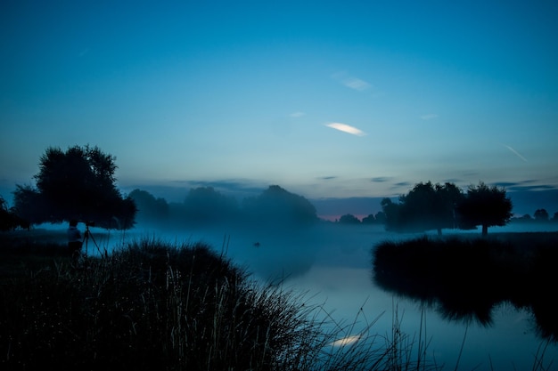 Las siluetas de los árboles y el lago contra el cielo azul