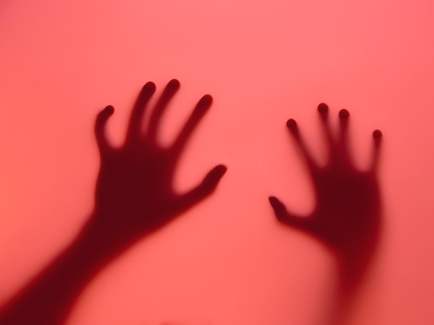 Siluetas de mãos pressionadas contra um fundo vermelho vívido