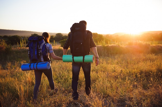 Siluetas de dos excursionistas con mochilas caminando al atardecer. Trekking y disfrutando de la vista del atardecer