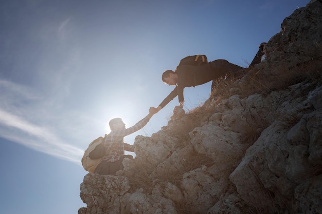 Siluetas de dos personas escalando montañas y ayudando contra el cielo azul