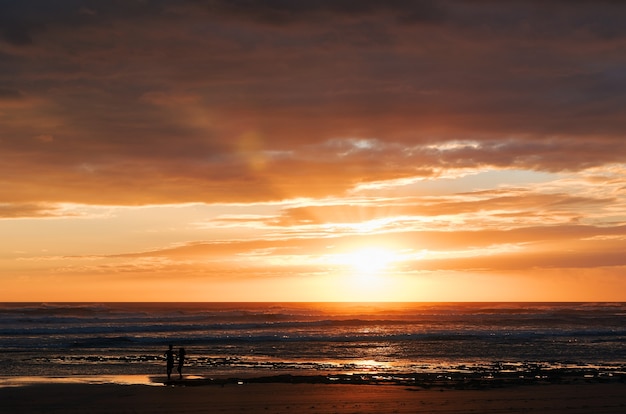 Siluetas de dos personas irreconocibles en la playa disfrutando de una hermosa puesta de sol
