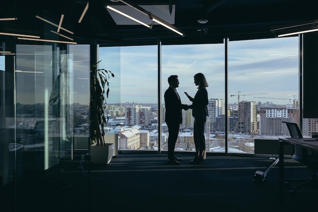 Siluetas de un equipo de dos empleados de hombres de negocios, hombres y mujeres asiáticos, están consultando y comunicándose trabajando en una oficina moderna junto a la ventana