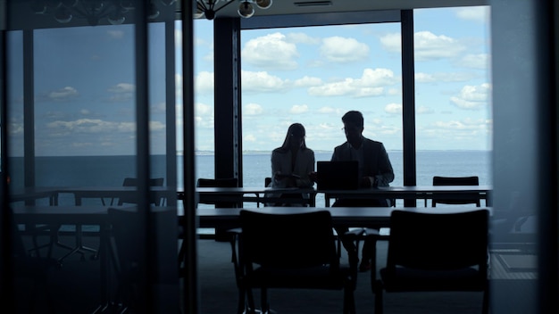 Siluetas de equipo de negocios hablando en la vista de las nubes del mar Dos gerentes trabajan portátil