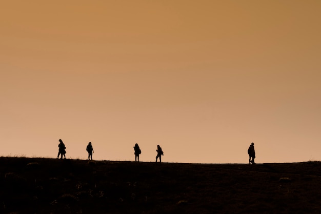 Siluetas de excursionistas con mochilas disfrutando de la vista del atardecer desde la cima de una montaña