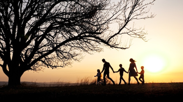 Siluetas de familia feliz caminando juntos en la pradera durante la puesta de sol