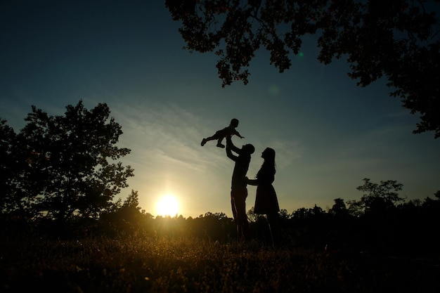 Siluetas de familia feliz, papá, mamá y bebé en la naturaleza en verano al atardecer con espacio para copiar texto