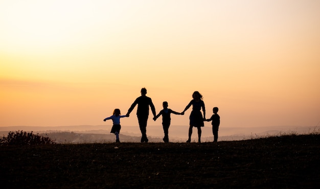 Siluetas de familia feliz tomados de la mano en la pradera durante la puesta de sol