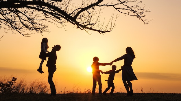 Siluetas de familia pasar tiempo juntos en la pradera cerca durante la puesta de sol