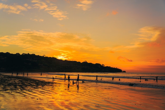 Siluetas de gran grupo de personas al atardecer naranja junto al mar