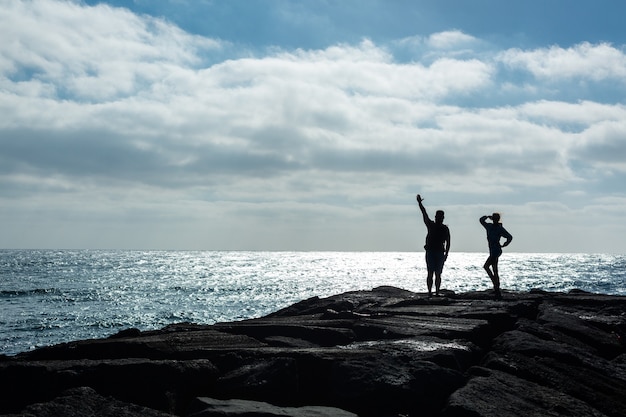 Siluetas de un hombre y una mujer en un muelle de piedra frente al océano. Isla de Lanzarote, España.