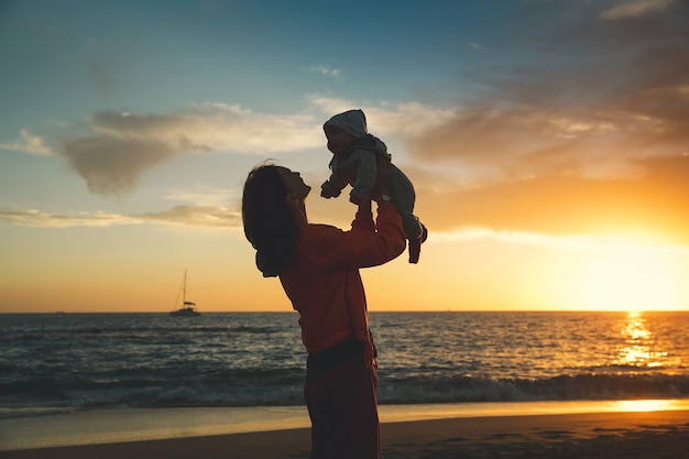 Siluetas de madre y bebé al atardecer en la playa del océano en verano Fondo familiar feliz