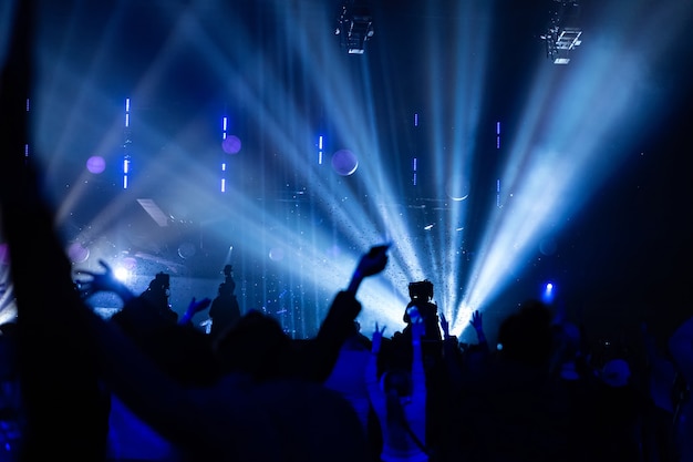 Siluetas de una multitud de conciertos y un camarógrafo en el contexto de rayos brillantes y coloridos en el escenario. la cámara con el operador está en la plataforma alta.