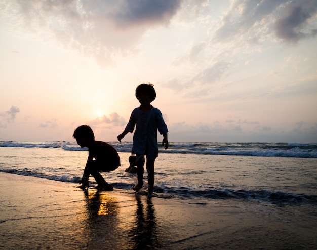 Siluetas de niños teniendo tiempo feliz en la playa del mar cerca de la puesta del sol