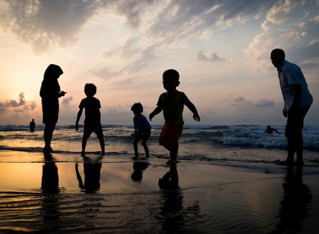 Siluetas de niños teniendo tiempo feliz en la playa del mar cerca de la puesta del sol