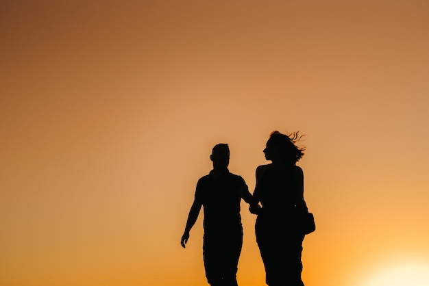 Siluetas de una pareja joven feliz chico y chica sobre un fondo de puesta de sol naranja en el desierto de arena