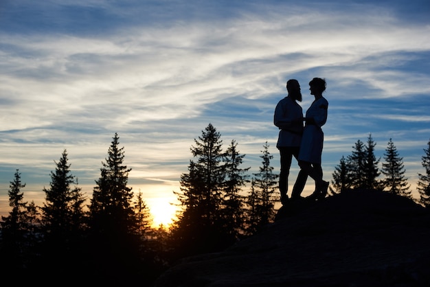 Siluetas de pareja joven sentada en la cima de la montaña en la noche