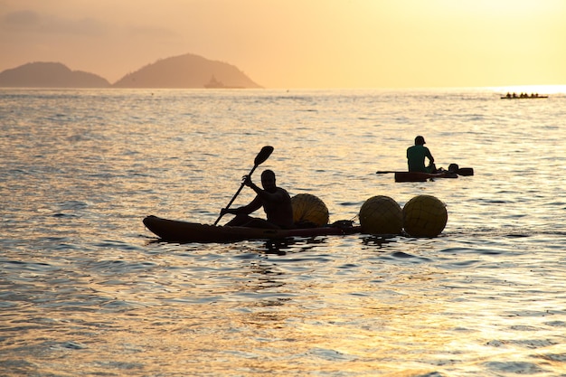 Siluetas de personas en canoas al amanecer en la playa de Copacabana en Río de Janeiro