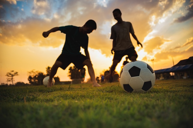 Siluetee el deporte de la acción al aire libre de un grupo de niños que se divierten jugando al fútbol del fútbol para el ejercicio.